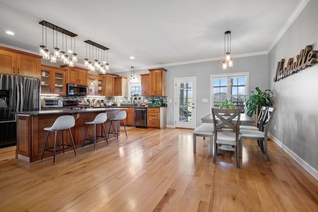 kitchen featuring crown molding, brown cabinets, light wood-style flooring, stainless steel appliances, and decorative backsplash