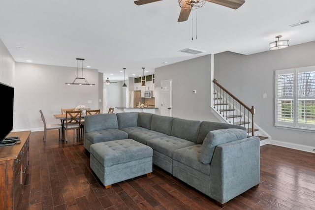 living area with dark wood-type flooring, ceiling fan, visible vents, and stairs