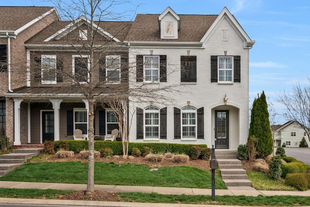 view of front of home with brick siding, a front lawn, a shingled roof, and covered porch