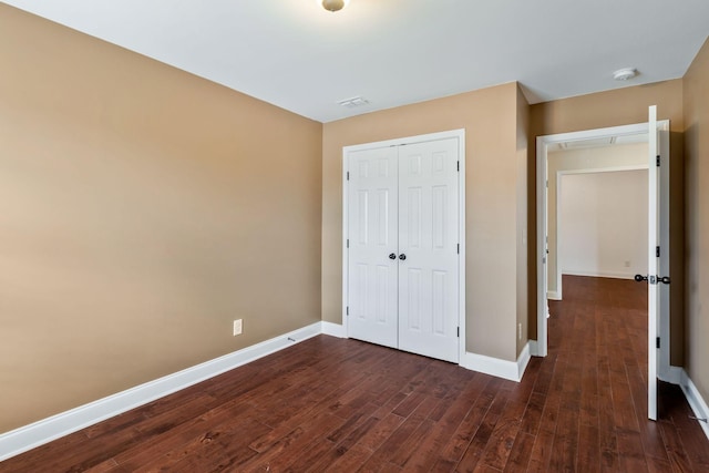 unfurnished bedroom with dark wood-style flooring, a closet, and baseboards