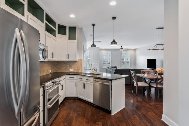 kitchen featuring open floor plan, a peninsula, dark countertops, appliances with stainless steel finishes, and a sink