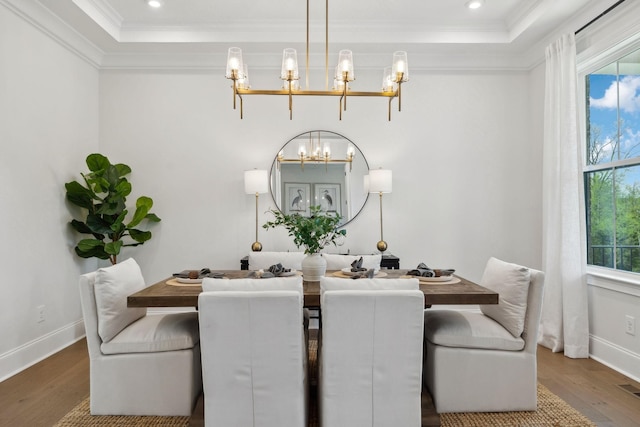dining room with a tray ceiling, ornamental molding, wood finished floors, and a chandelier