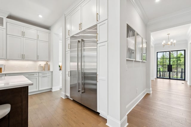 kitchen with stainless steel built in refrigerator, crown molding, a chandelier, and light wood-type flooring