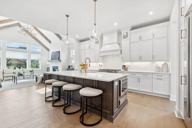 kitchen featuring light countertops, light wood-type flooring, premium range hood, backsplash, and a sink