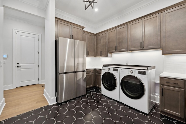 washroom with baseboards, ornamental molding, dark wood-type flooring, washer and dryer, and cabinet space