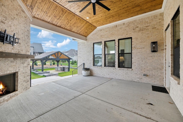 view of patio featuring an outdoor brick fireplace, a gazebo, and a ceiling fan
