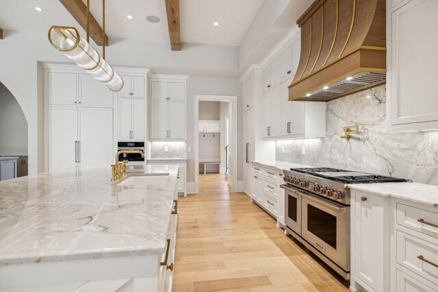 8115 Devens Dr, Brentwood, TN 37027 - kitchen featuring premium range hood, beam ceiling, arched walkways, appliances with stainless steel finishes, and light wood-type flooring