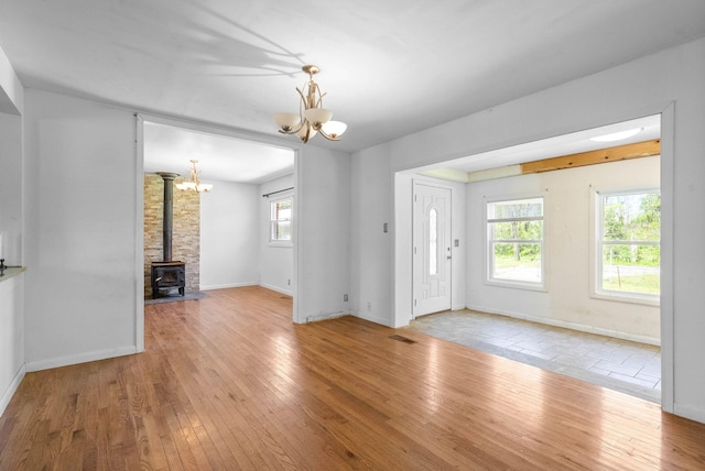 unfurnished living room featuring hardwood / wood-style floors, a wood stove, visible vents, baseboards, and a notable chandelier