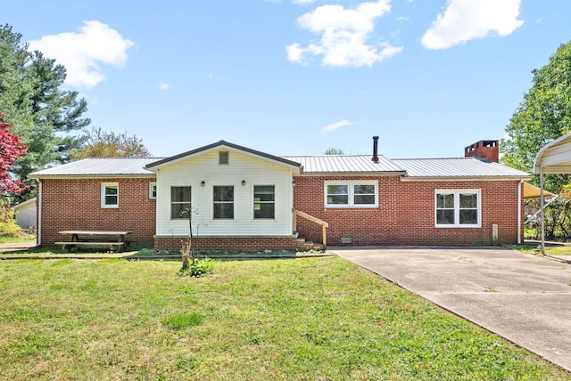 back of house featuring a chimney, concrete driveway, a lawn, metal roof, and brick siding