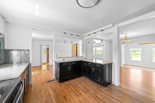 kitchen with dark cabinetry, an inviting chandelier, a wealth of natural light, and light wood finished floors