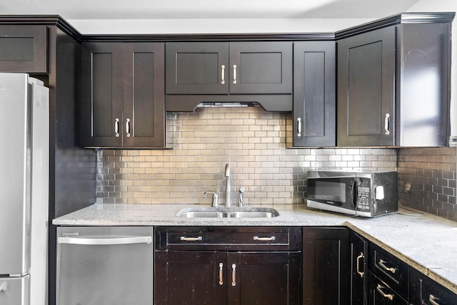 kitchen with light stone counters, dark brown cabinets, a sink, decorative backsplash, and stainless steel appliances