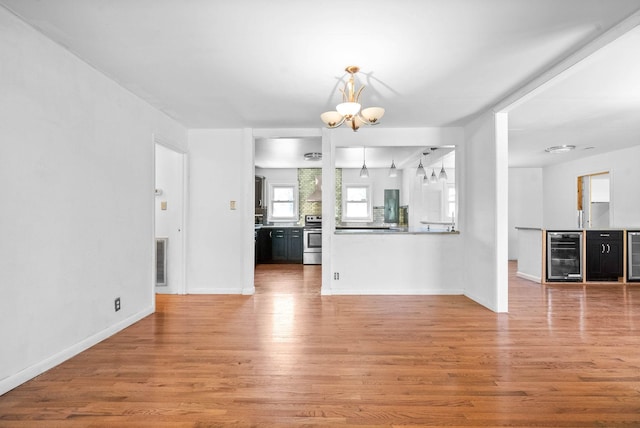 unfurnished living room with light wood-type flooring, visible vents, a notable chandelier, and wine cooler