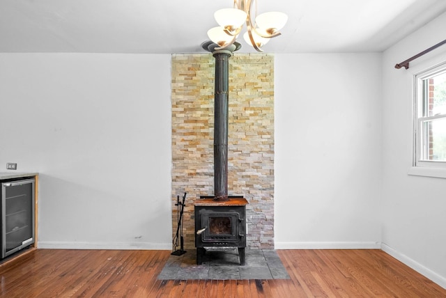 unfurnished living room with wine cooler, baseboards, a chandelier, wood finished floors, and a wood stove