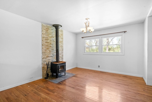 unfurnished living room featuring light wood finished floors, baseboards, a chandelier, and a wood stove