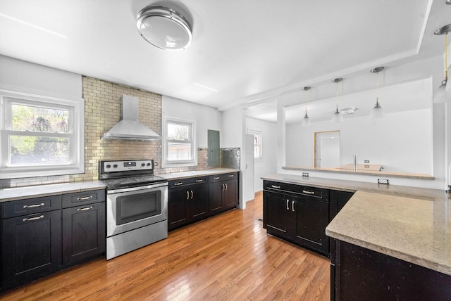 kitchen featuring backsplash, wall chimney range hood, dark cabinetry, light wood-type flooring, and electric range