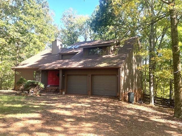 view of front of property featuring dirt driveway, a chimney, and an attached garage
