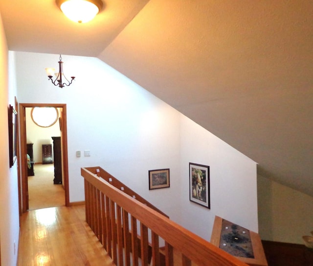 hall featuring lofted ceiling, an upstairs landing, a chandelier, and light wood finished floors