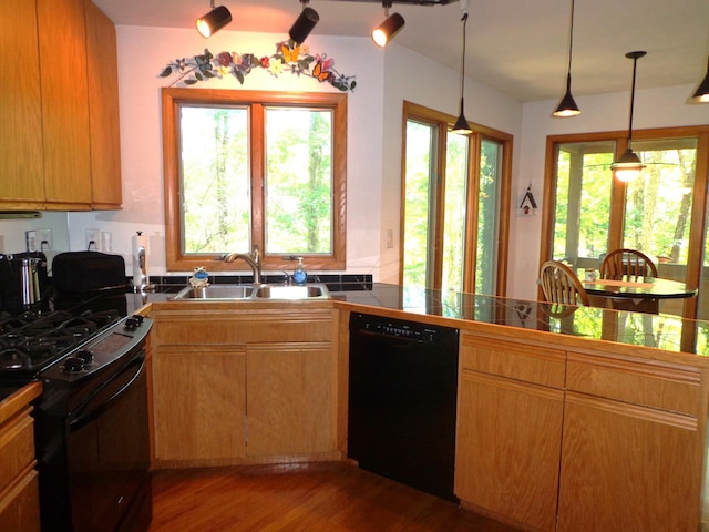 kitchen featuring wood finished floors, dark countertops, a sink, decorative light fixtures, and black appliances