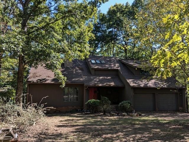 view of front of property featuring dirt driveway, a shingled roof, and a garage