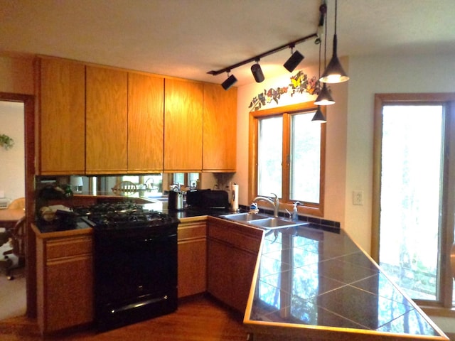 kitchen featuring a sink, tile counters, a peninsula, hanging light fixtures, and gas stove