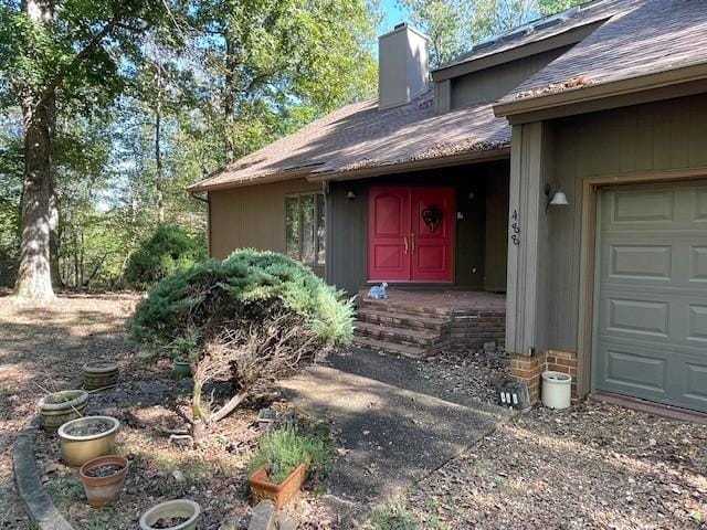 doorway to property with a chimney, a garage, and roof with shingles