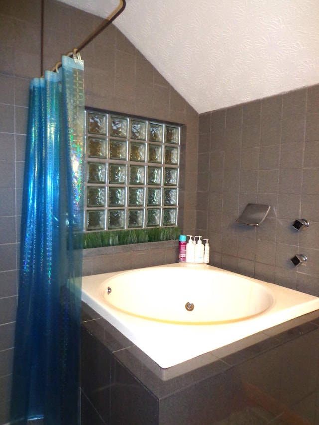 full bathroom with a bath, tile walls, a textured ceiling, a tile shower, and lofted ceiling
