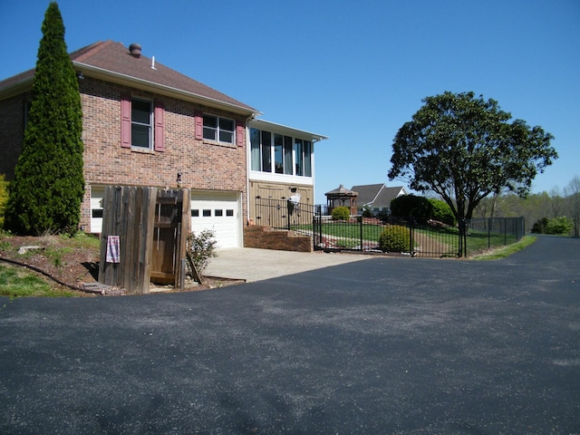 view of property exterior featuring driveway, a garage, fence, and brick siding