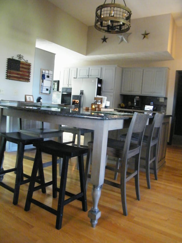 kitchen with a towering ceiling, a kitchen breakfast bar, an inviting chandelier, light wood-style floors, and black appliances