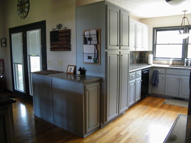 kitchen featuring light wood-type flooring, gray cabinets, decorative light fixtures, dishwasher, and a sink