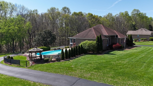 view of swimming pool with a gazebo, a forest view, fence, and a lawn