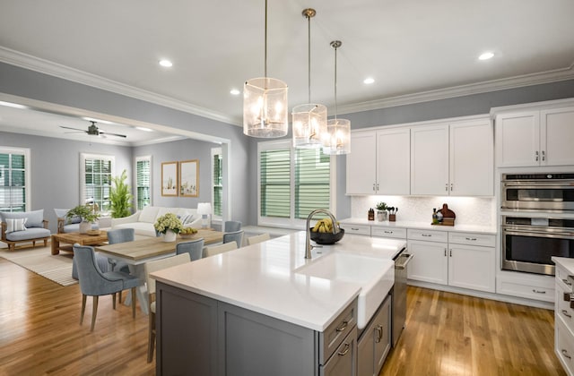 kitchen with open floor plan, stainless steel appliances, white cabinetry, and light wood-type flooring