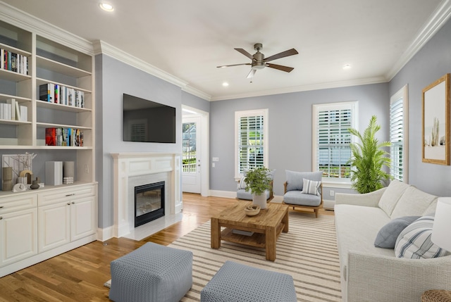 living area featuring recessed lighting, ornamental molding, light wood-style floors, a premium fireplace, and ceiling fan