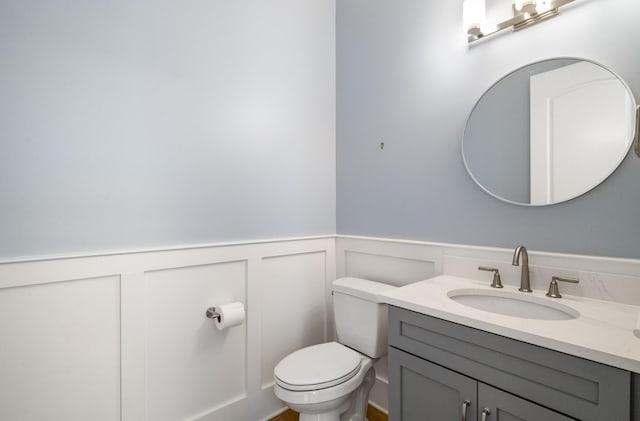 bathroom featuring vanity, toilet, a wainscoted wall, and a decorative wall