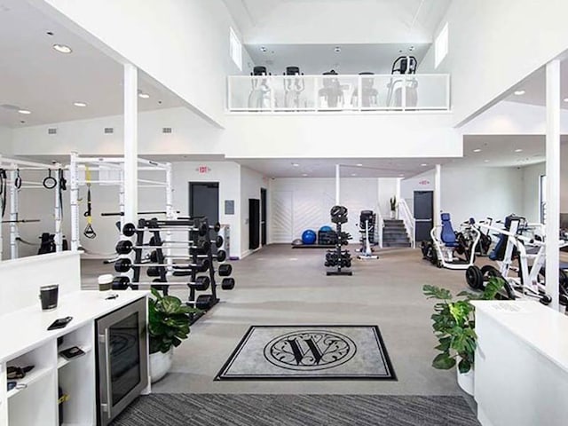 exercise room with a towering ceiling, carpet flooring, wine cooler, visible vents, and recessed lighting