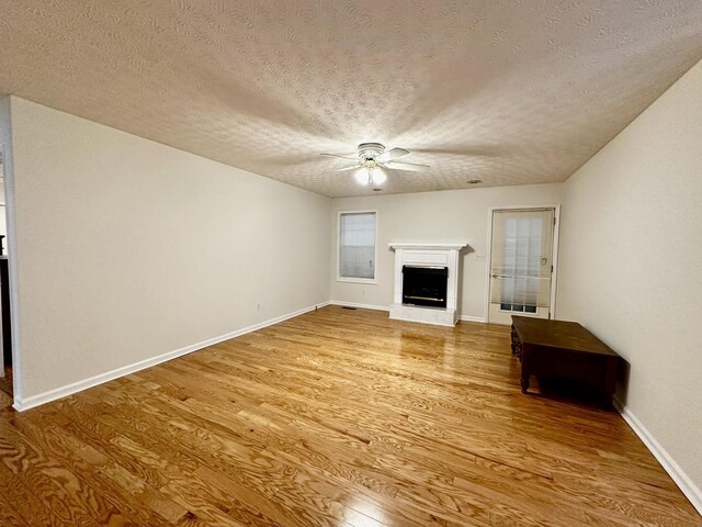 273 Chapel Rd, New Johnsonville, TN 37134 - unfurnished living room featuring a ceiling fan, light wood finished floors, a fireplace with raised hearth, a textured ceiling, and baseboards