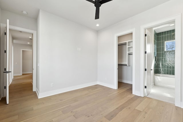 unfurnished bedroom featuring ensuite bathroom, baseboards, light wood-style floors, and a walk in closet