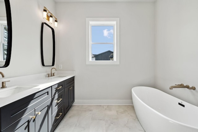 bathroom with a freestanding bath, baseboards, a sink, and double vanity
