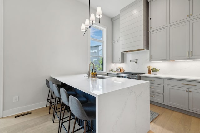 kitchen featuring stove, visible vents, a sink, gray cabinetry, and a kitchen bar