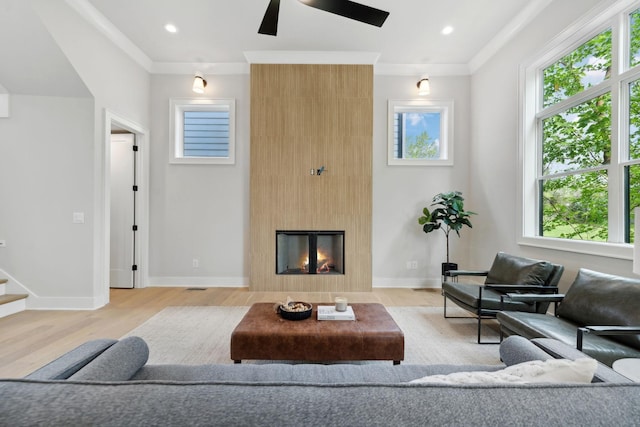 living area featuring ornamental molding, baseboards, a ceiling fan, and light wood-style flooring