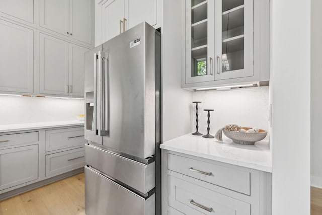 kitchen with light stone counters, glass insert cabinets, light wood-type flooring, stainless steel fridge with ice dispenser, and gray cabinetry