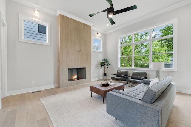 living room featuring visible vents, ornamental molding, baseboards, light wood-style flooring, and a large fireplace