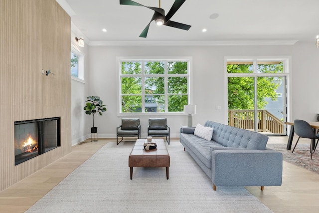 living area featuring light wood-style flooring, recessed lighting, a large fireplace, ceiling fan, and crown molding