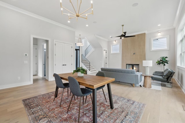 dining area featuring stairway, ornamental molding, baseboards, light wood-style flooring, and ceiling fan with notable chandelier