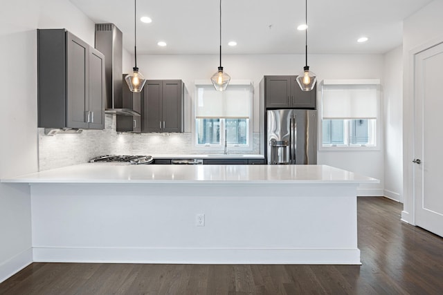 kitchen with tasteful backsplash, stainless steel refrigerator with ice dispenser, gray cabinets, wall chimney range hood, and a peninsula