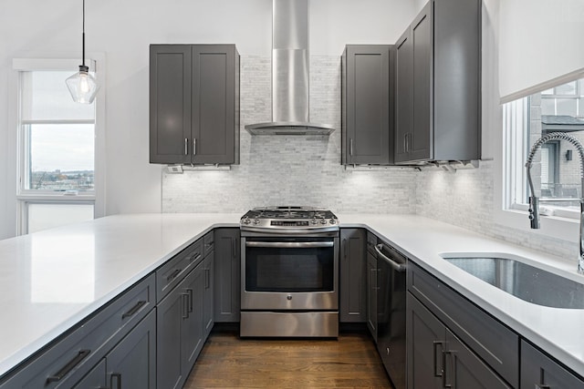 kitchen with light countertops, stainless steel appliances, dark wood finished floors, a sink, and wall chimney range hood