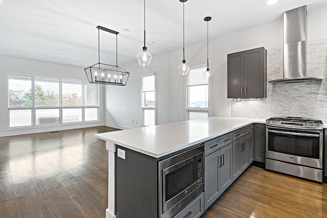 kitchen featuring a peninsula, wall chimney exhaust hood, appliances with stainless steel finishes, dark wood-style floors, and gray cabinets