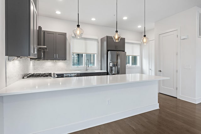kitchen with light countertops, a sink, dark wood-style floors, a peninsula, and appliances with stainless steel finishes