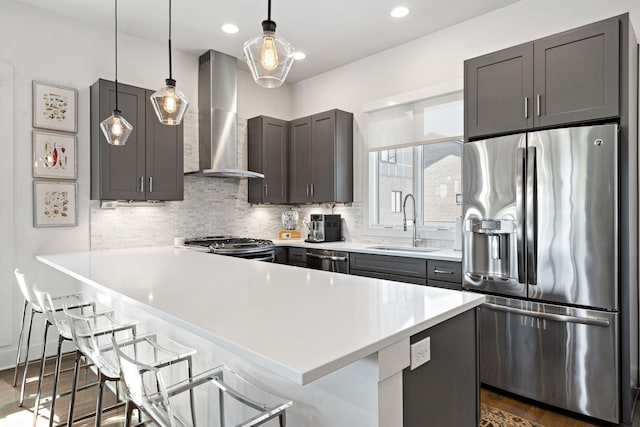 kitchen with light countertops, a sink, wall chimney exhaust hood, a kitchen breakfast bar, and stainless steel appliances