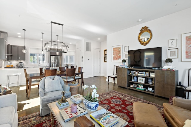 living room featuring dark wood-type flooring, baseboards, visible vents, recessed lighting, and an inviting chandelier