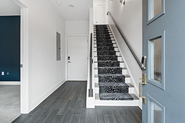 stairs featuring wood finish floors, baseboards, and electric panel